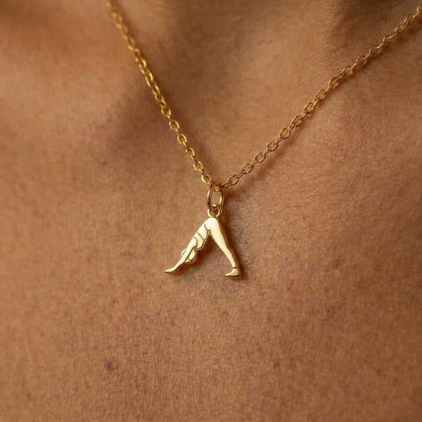 Small gold pendant of a figure in downward dog pose on a fine chain, white background.