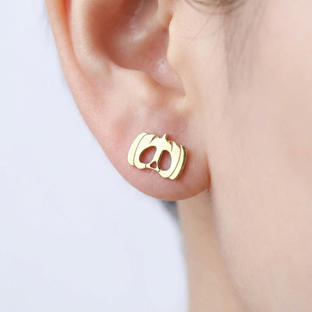 Two mismatched tiny gold Halloween mask stud earrings, pumpkin and vampire faces