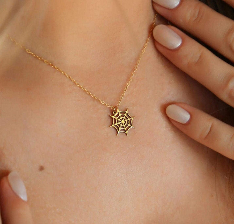 Dainty gold spider web pendant with fine radial threads, hanging from a thin gold-filled cable chain