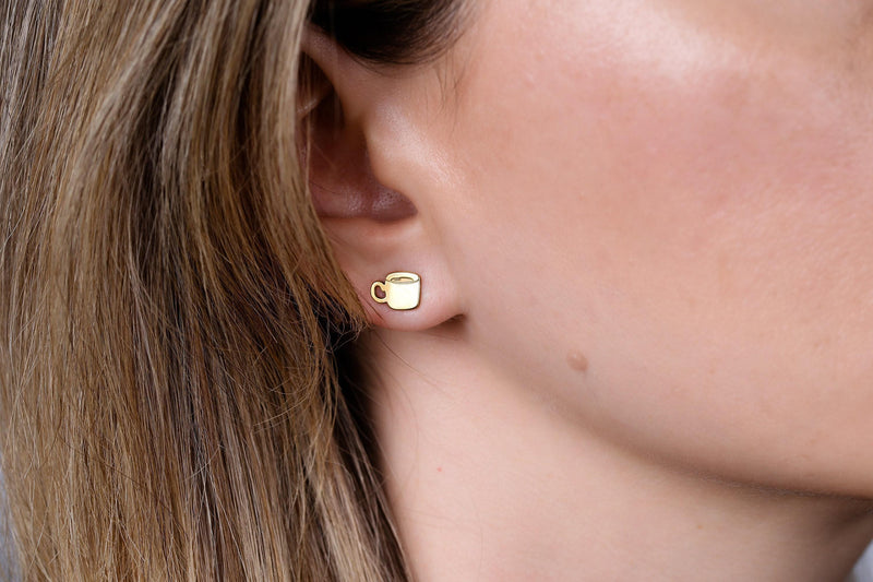 Pair of tiny gold coffee cup stud earrings with handle and steam, on white