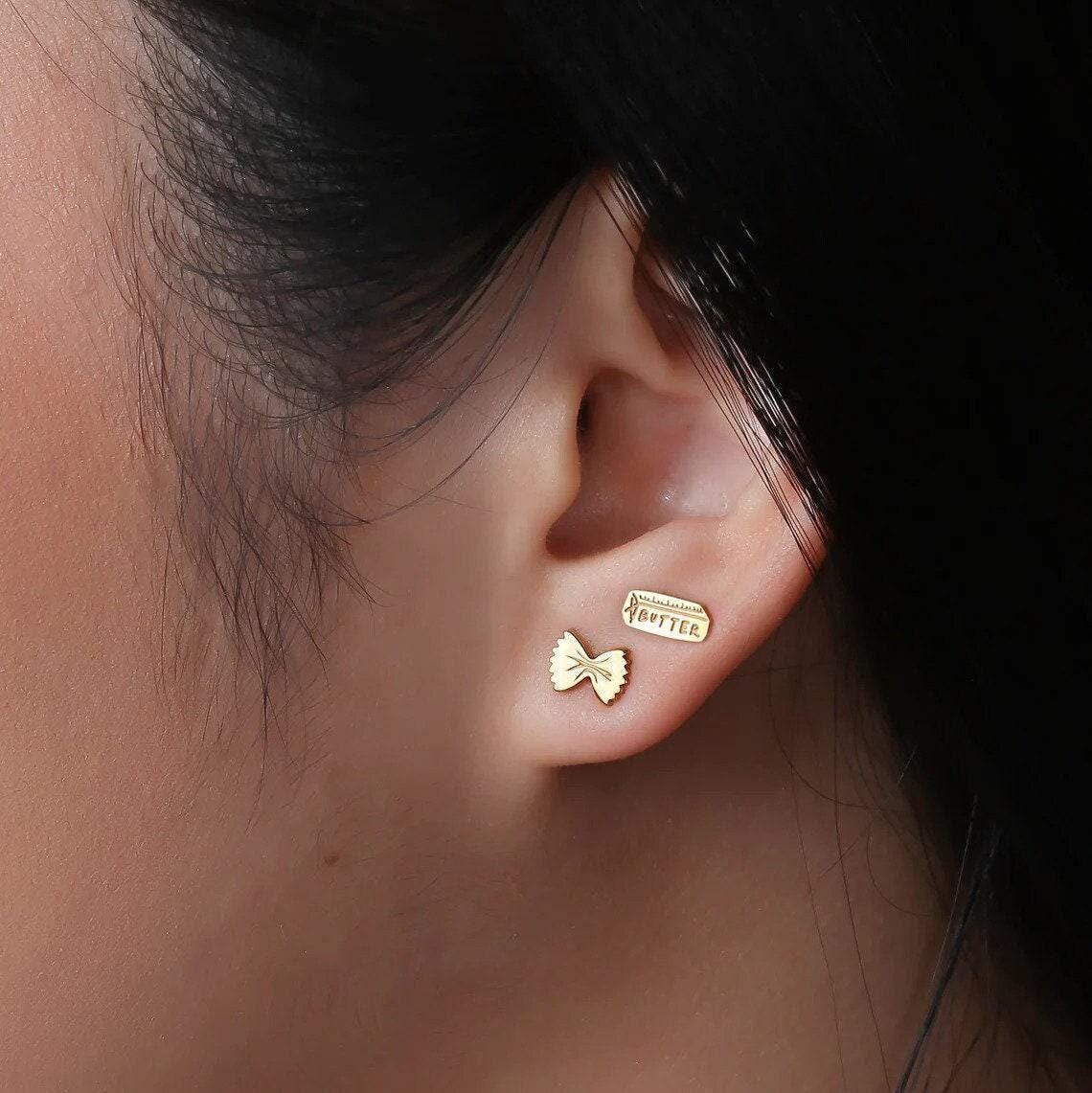 Mismatched gold stud earrings, a butter pat and a pasta twist