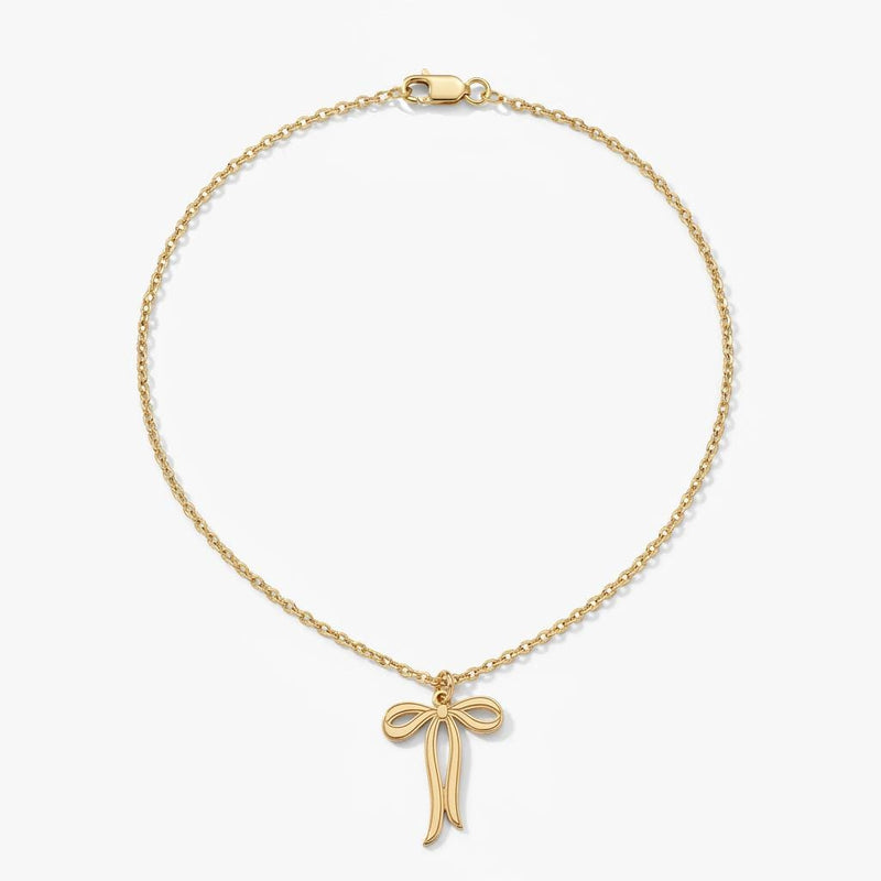 Slim gold ribbon bow pendant with trailing tails on a fine chain, white background.