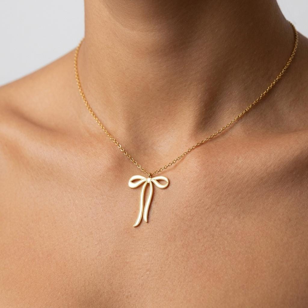 Slim gold ribbon bow pendant with trailing tails on a fine chain, white background. (2 of 9)