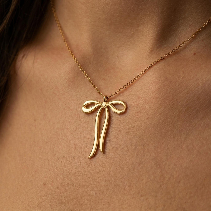 Slim gold ribbon bow pendant with trailing tails on a fine chain, white background. (3 of 9)