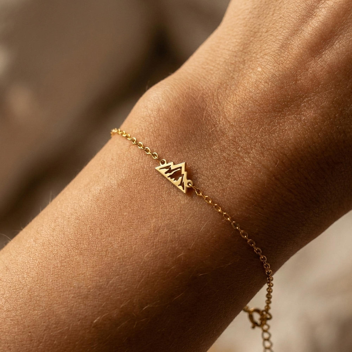 Fine gold chain bracelet with a small mountain range charm and extender on a wrist