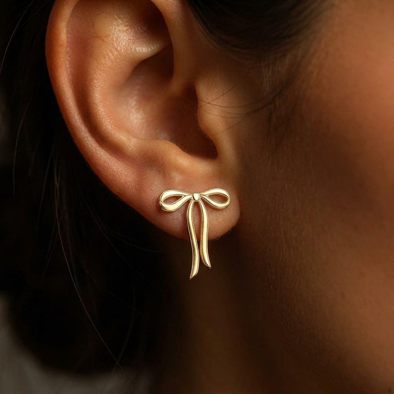 Pair of gold ribbon bow stud earrings shown flat on a white background.