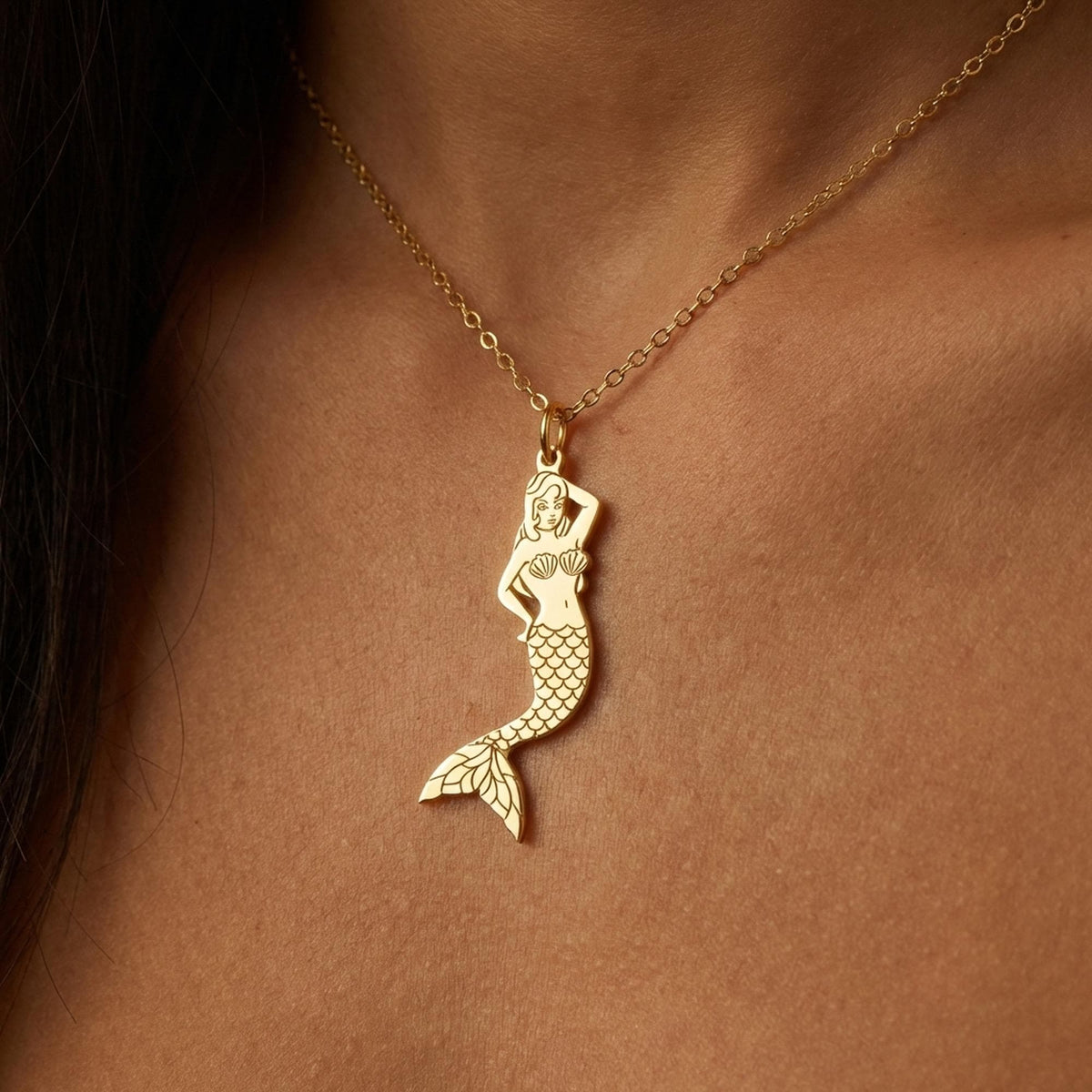 Small gold mermaid pendant with curled tail and sweeping hair on a thin chain