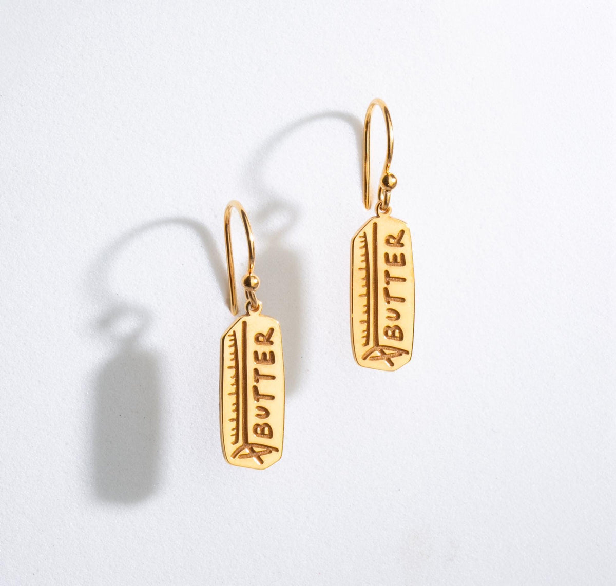Pair of gold butter stick drop earrings hanging from small posts