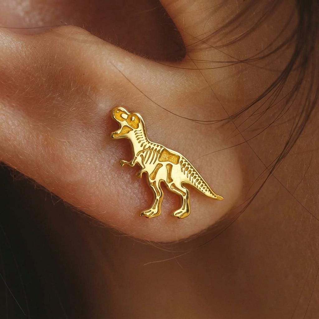 Pair of gold stud earrings shaped like a T-rex skull in profile