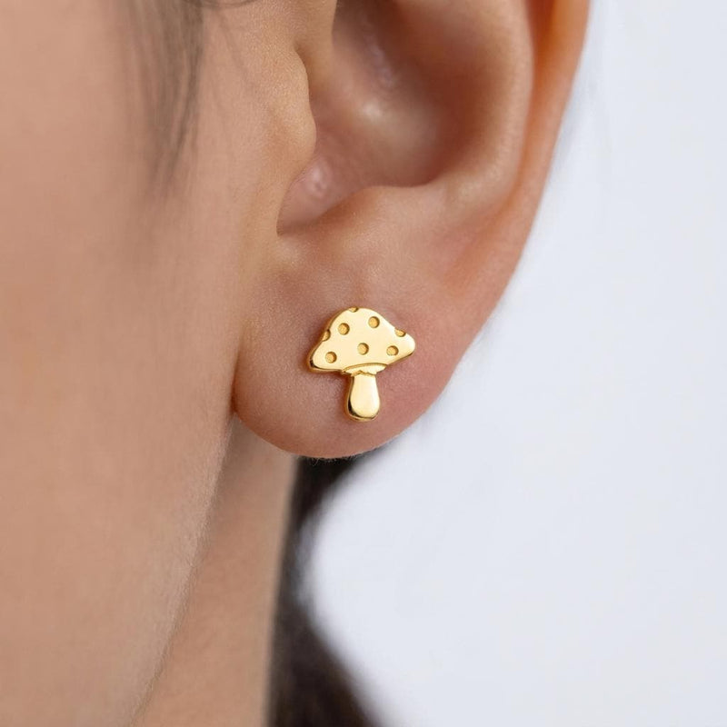 Pair of tiny gold mushroom stud earrings with spotted caps on white