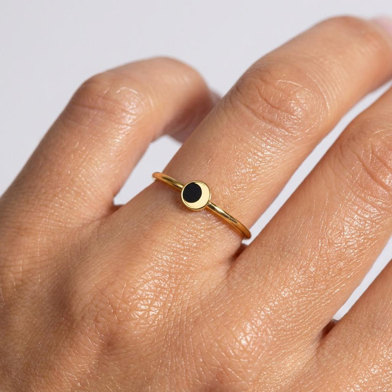 Thin gold stacking ring with a small half-black eclipse disc on the crown