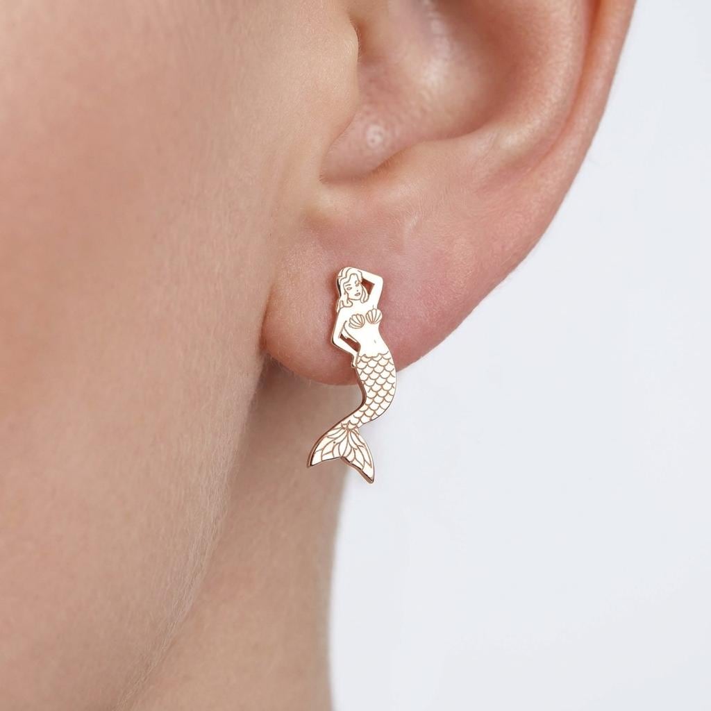 Pair of small gold mermaid stud earrings with curved tails on a white background.