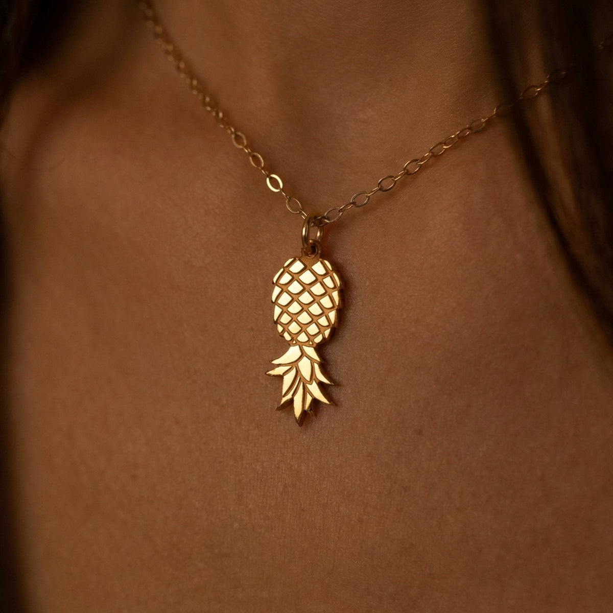 Fine gold chain necklace with a small pineapple pendant hanging point down