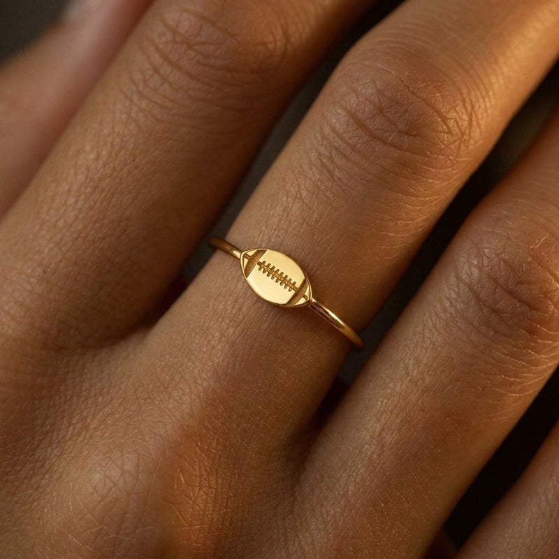 Gold ring with a small football charm with cut laces set flat on a thin band