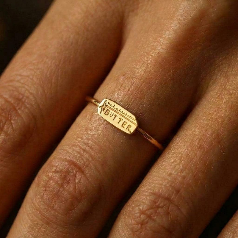 Gold ring with a small butter stick charm sitting flat on a thin round band