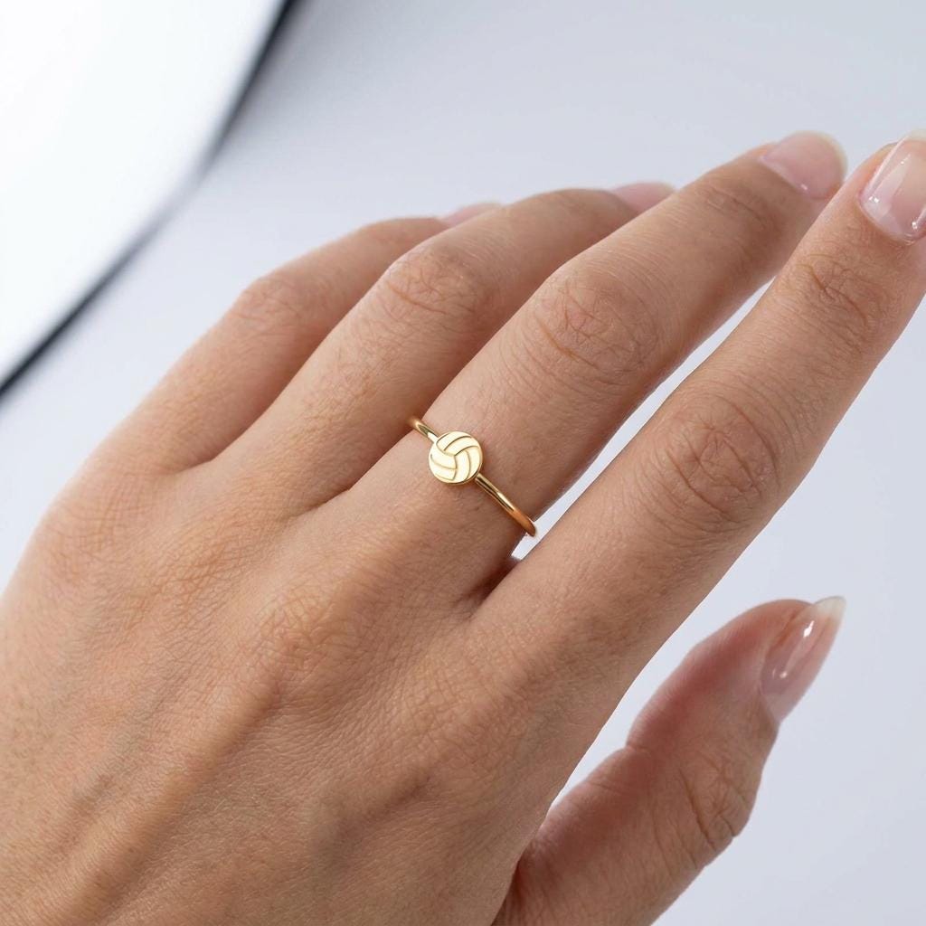 Thin gold stacking ring with a tiny volleyball charm sitting flat on the band