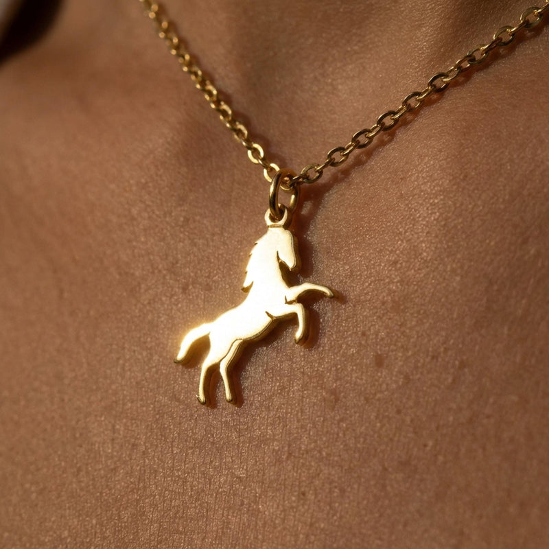 Fine gold chain necklace with a small running horse pendant on a plain background