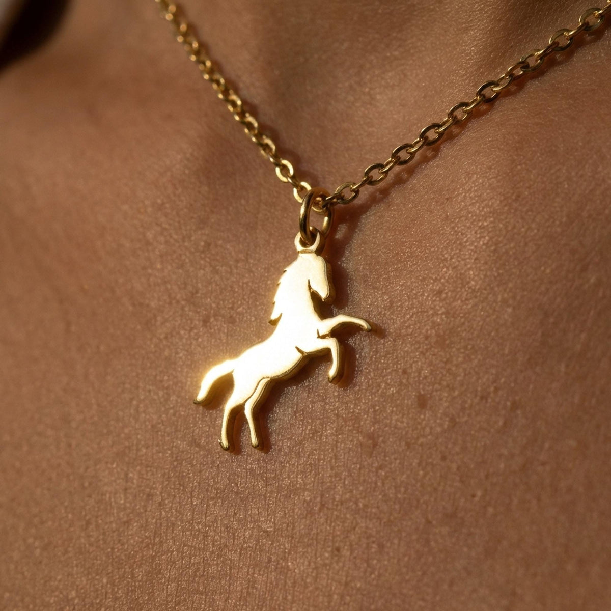 Fine gold chain necklace with a small running horse pendant on a plain background