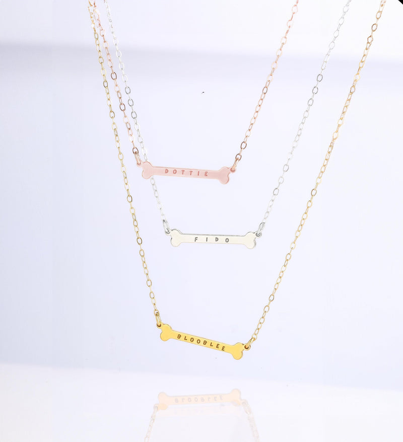 Small gold dog bone pendant on a fine chain, shown against a plain backdrop.