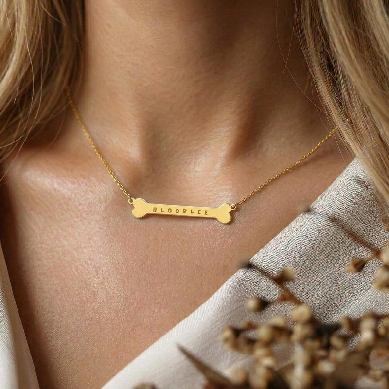 Small gold dog bone pendant on a fine chain, shown against a plain backdrop. (2 of 7)