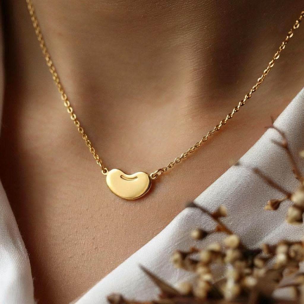 Tiny gold bean pendant on a delicate cable chain against a white background. (2 of 6)