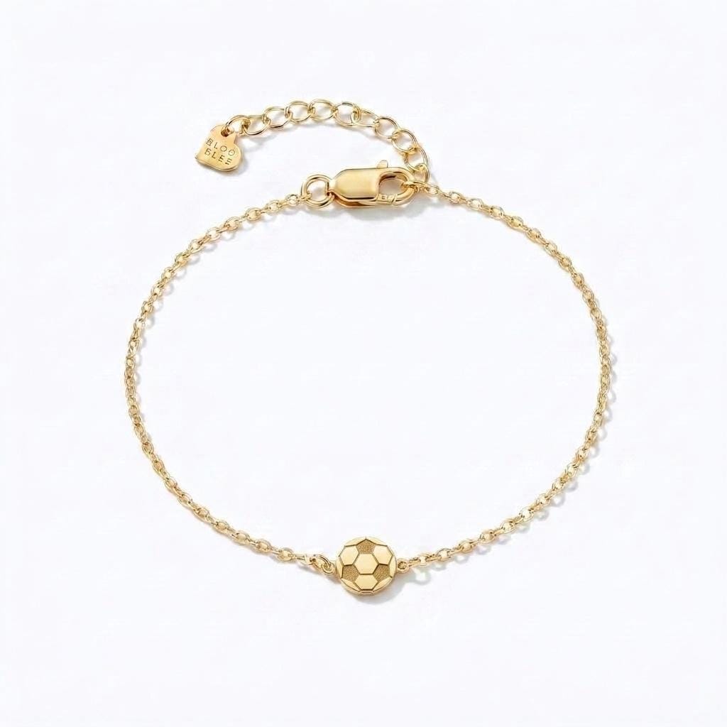 Fine gold chain bracelet with a small soccer ball charm and extender on a wrist