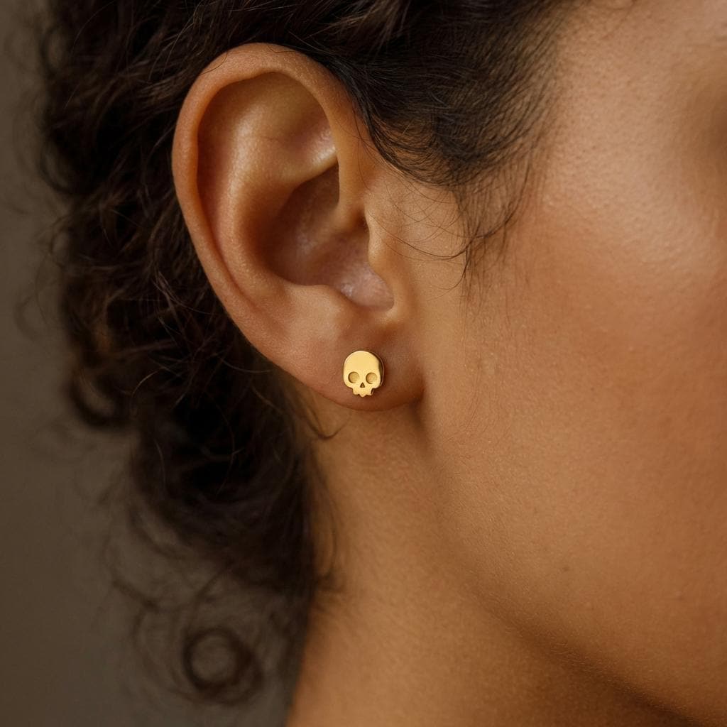 Pair of tiny gold skull stud earrings with cut eye sockets and jaws