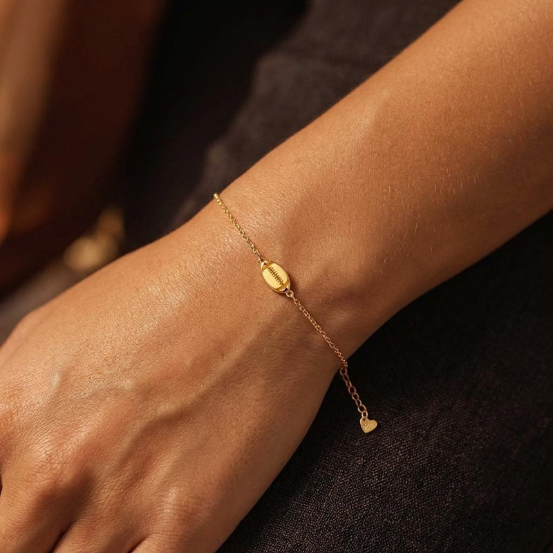 Thin gold chain bracelet with a small football charm showing laces