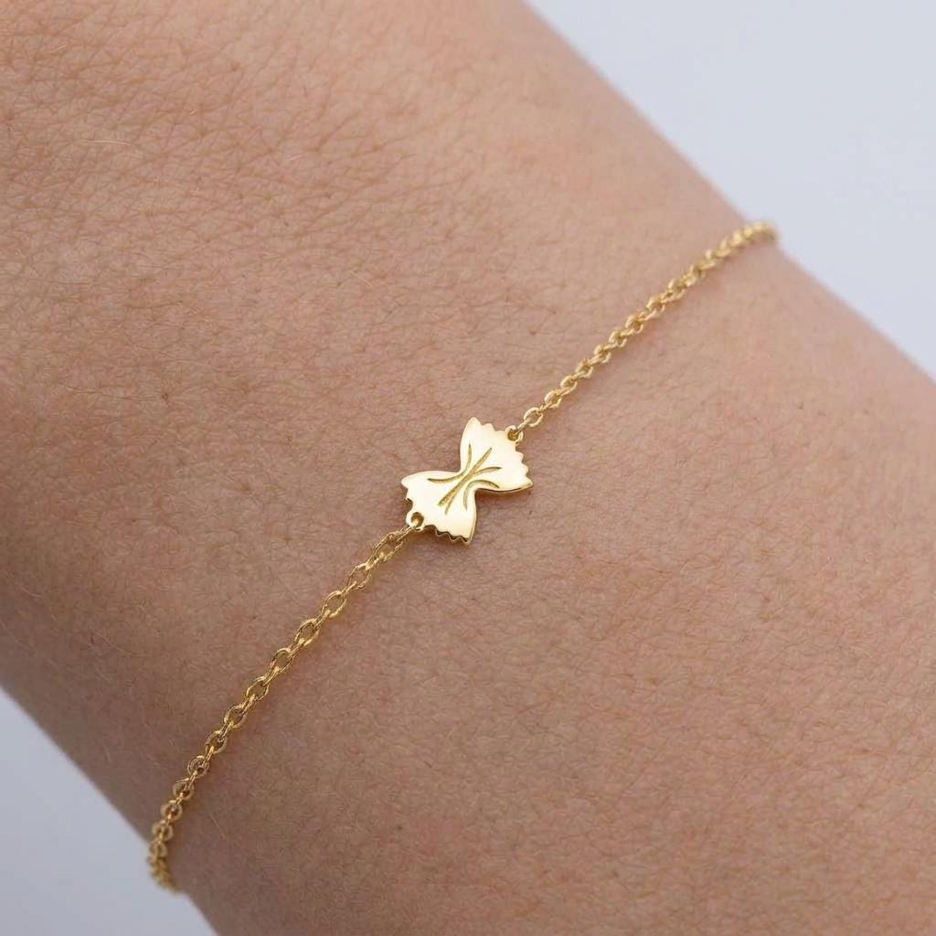 Tiny gold bowtie pasta charm on a fine cable chain bracelet