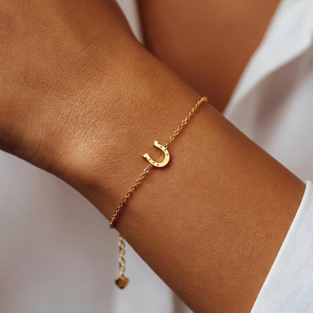 Fine chain bracelet with a small flat gold horseshoe charm.