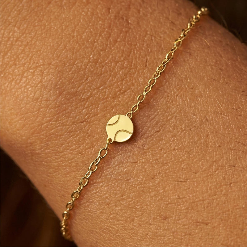 Fine gold chain bracelet with a very small round tennis ball charm