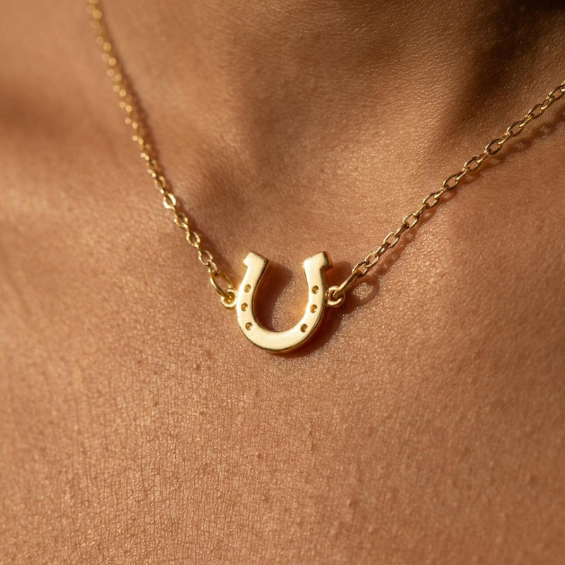 Tiny gold horseshoe pendant with nail holes on a fine chain