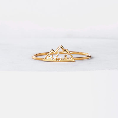 Thin gold stacking ring with a small flat mountain peak across the top, on a hand