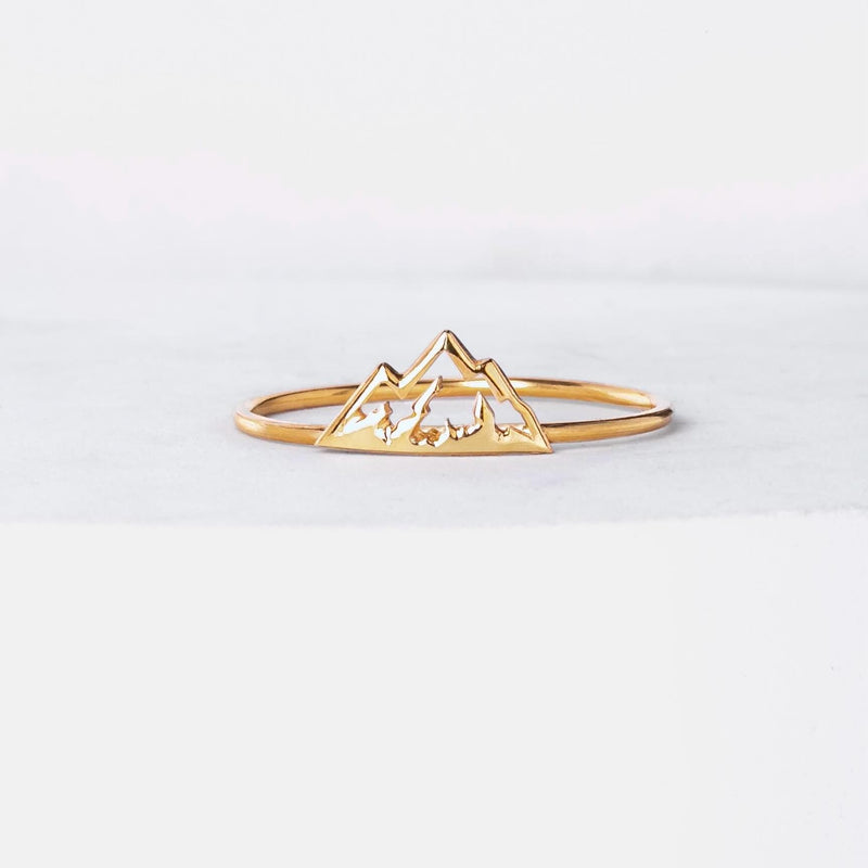 Thin gold stacking ring with a small flat mountain peak across the top, on a hand