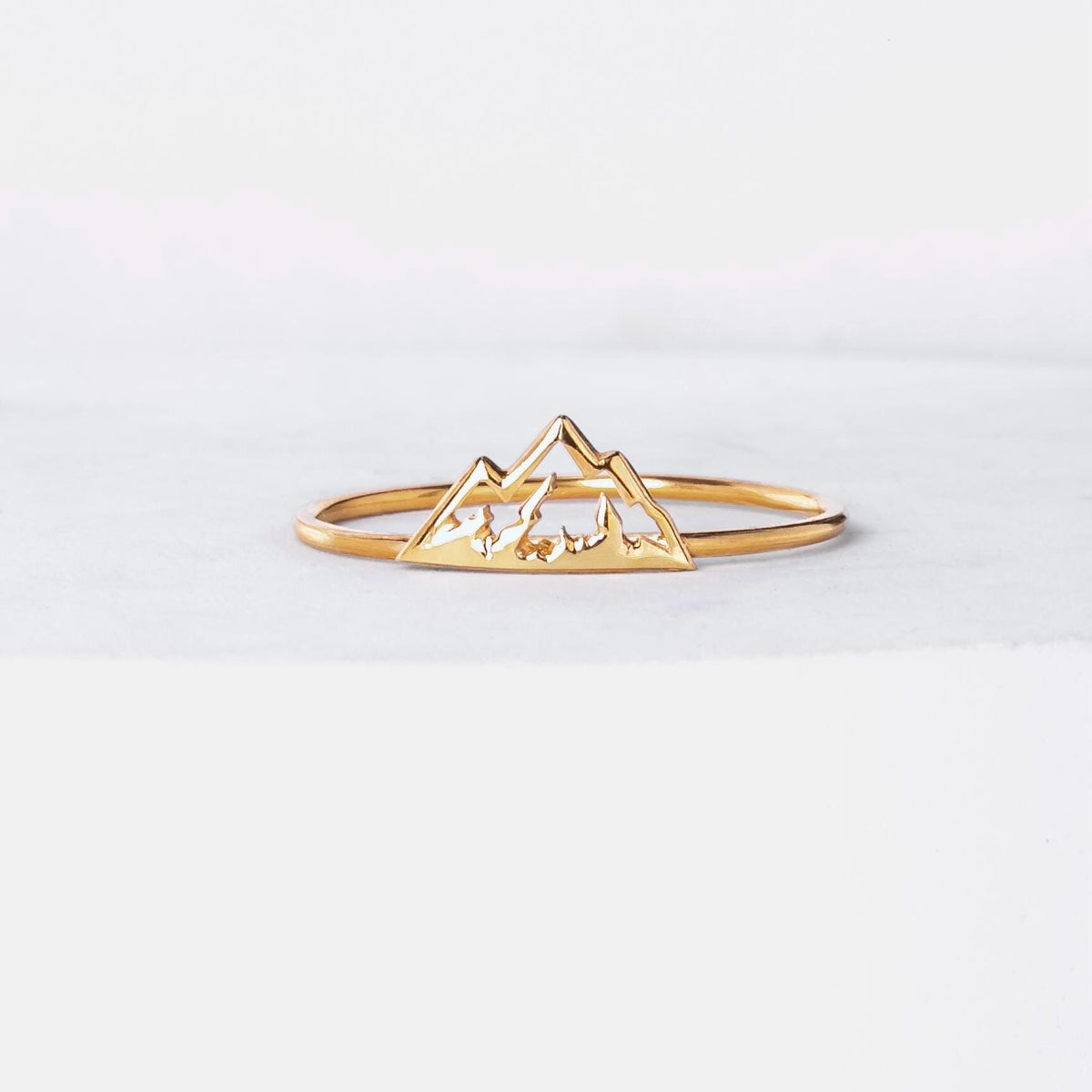 Thin gold stacking ring with a small flat mountain peak across the top, on a hand