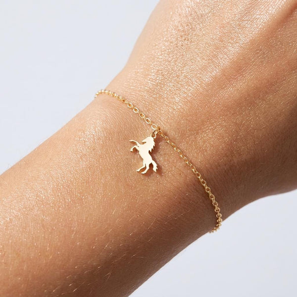Fine gold chain bracelet with a tiny horse charm and lobster clasp on a wrist