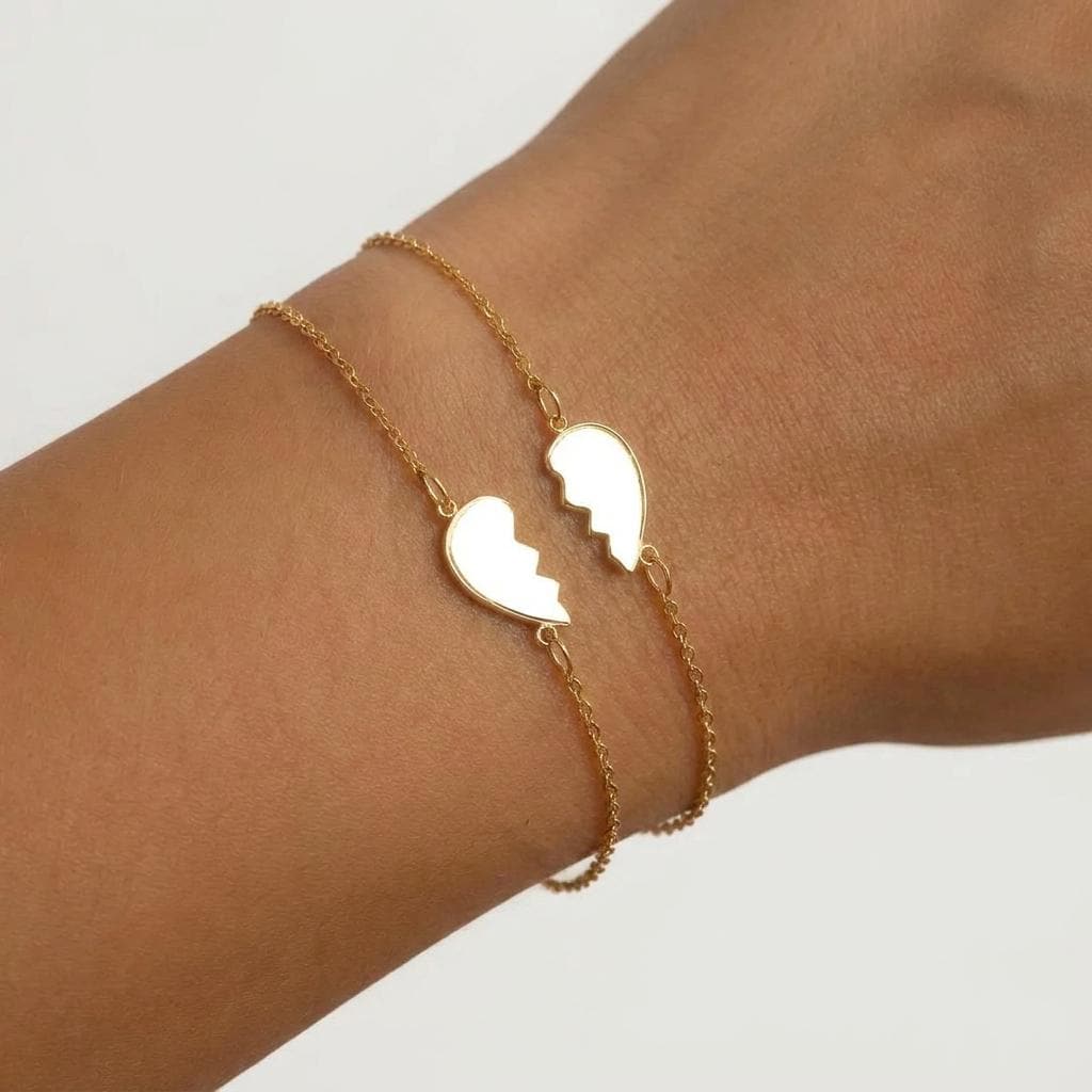 Two gold bracelets each holding one half of a split heart charm on fine cable chain