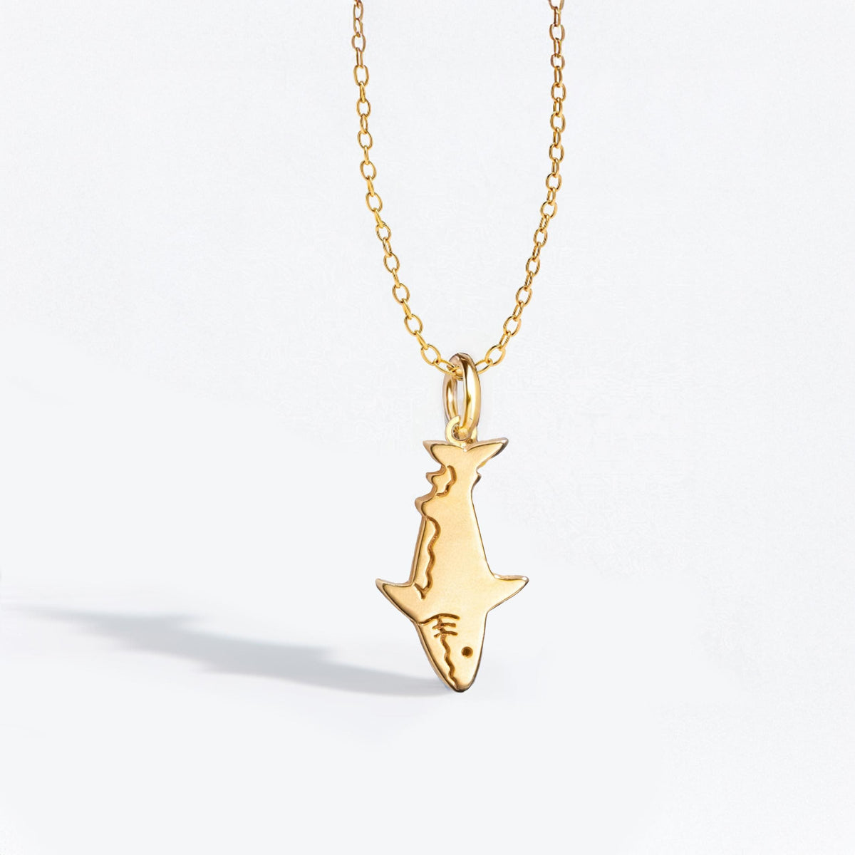 Fine gold chain necklace with a small shark pendant shown in profile