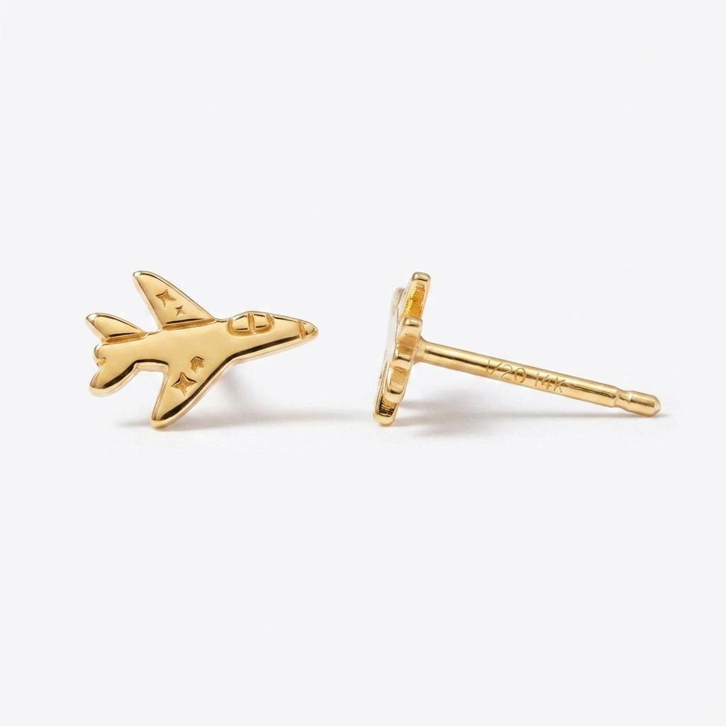 Pair of small gold fighter jet stud earrings with swept wings on a white background