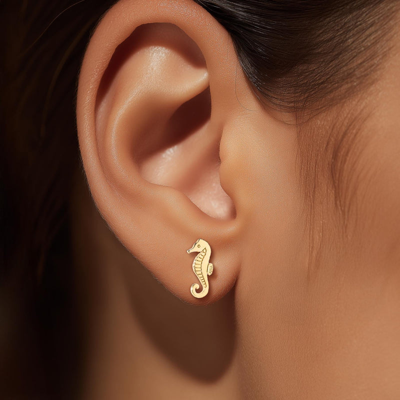 Pair of small gold seahorse stud earrings with curled tails.