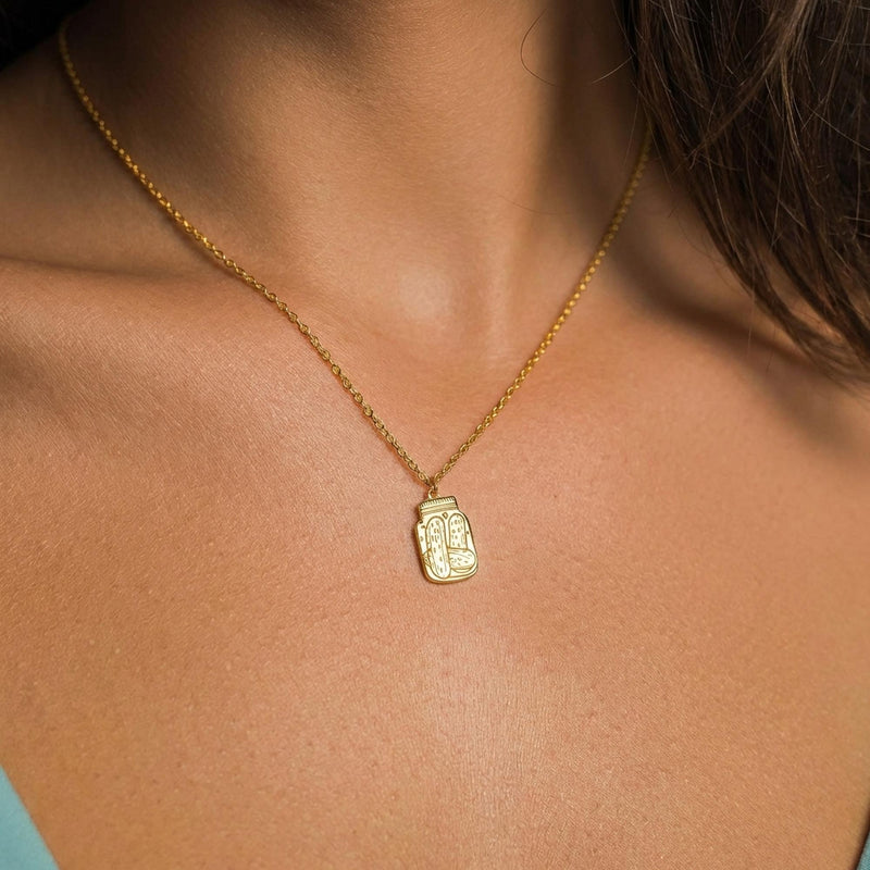 Fine gold chain necklace with a small pickle jar pendant on a plain background (2 of 8)