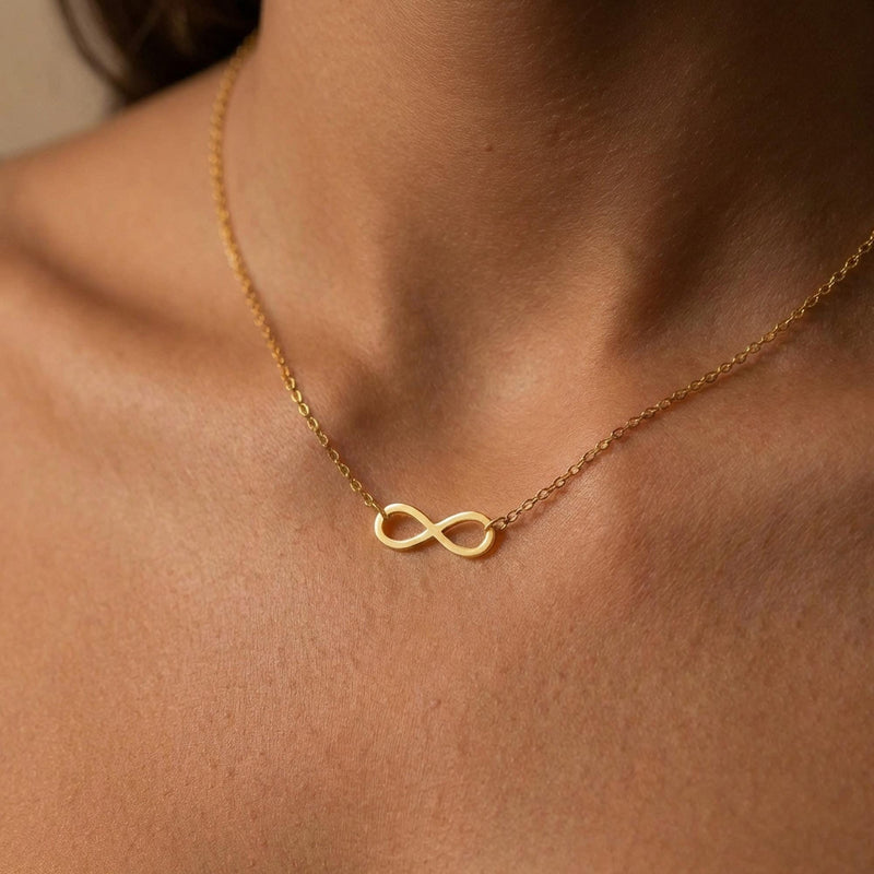 Small gold infinity loop pendant lying flat on a fine cable chain