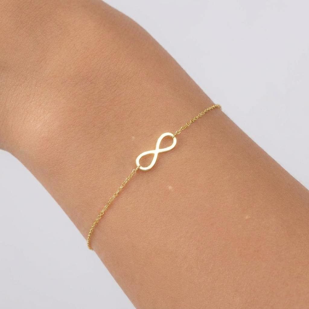Fine chain bracelet with a small flat gold infinity loop charm at the center.