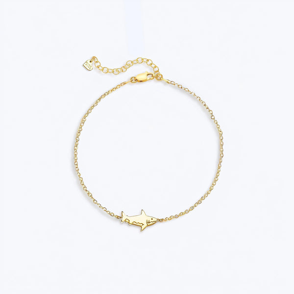 Tiny gold shark charm in profile on a fine cable chain bracelet