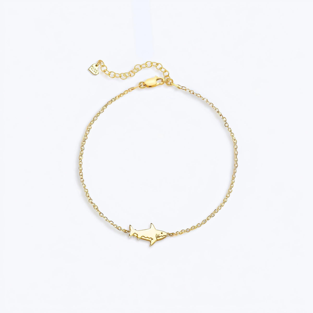Tiny gold shark charm in profile on a fine cable chain bracelet