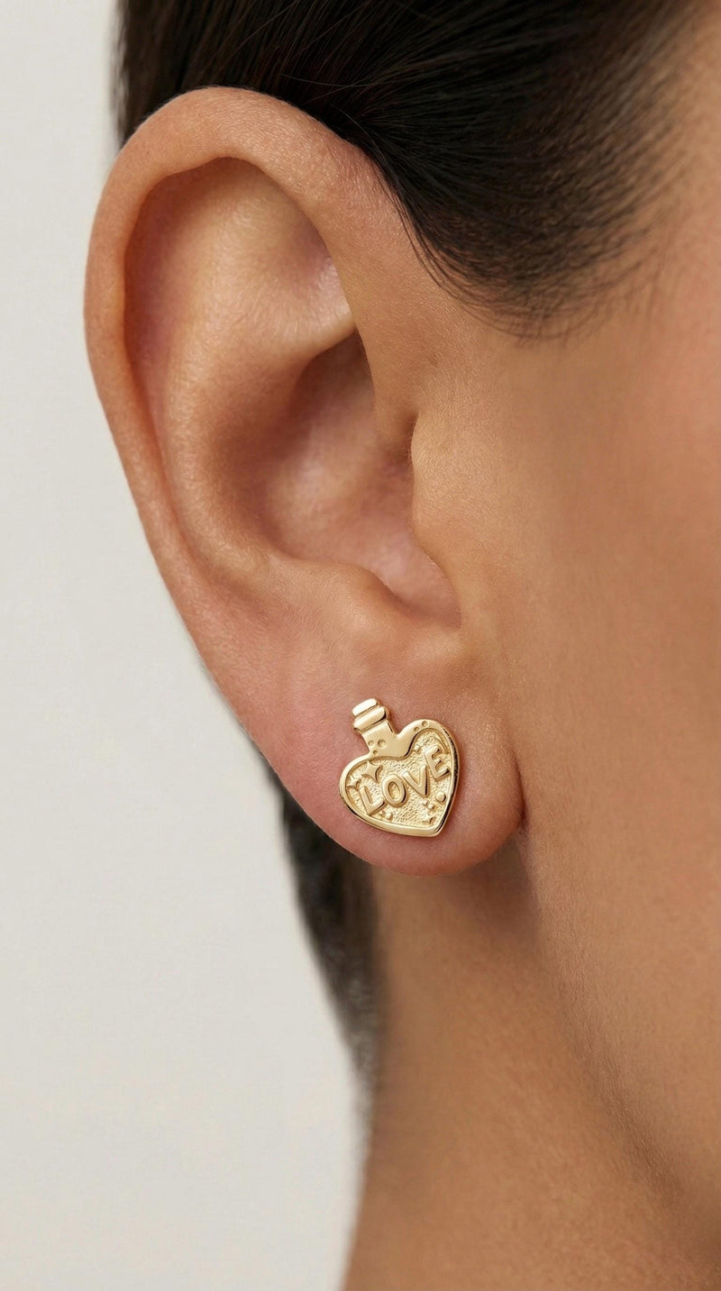 Pair of tiny gold love potion bottle stud earrings with heart labels, white background. (2 of 6)