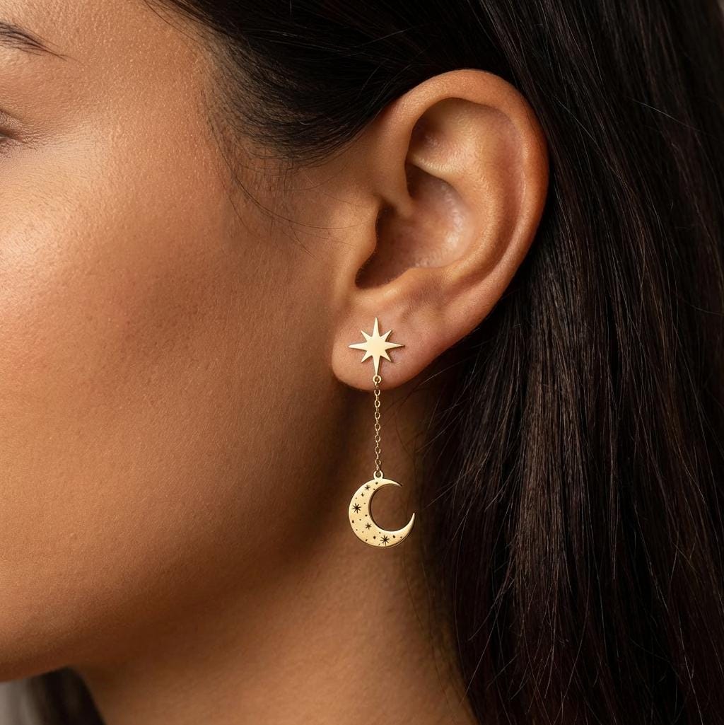 Pair of gold crescent moon and star drop earrings with black ink detail, on white