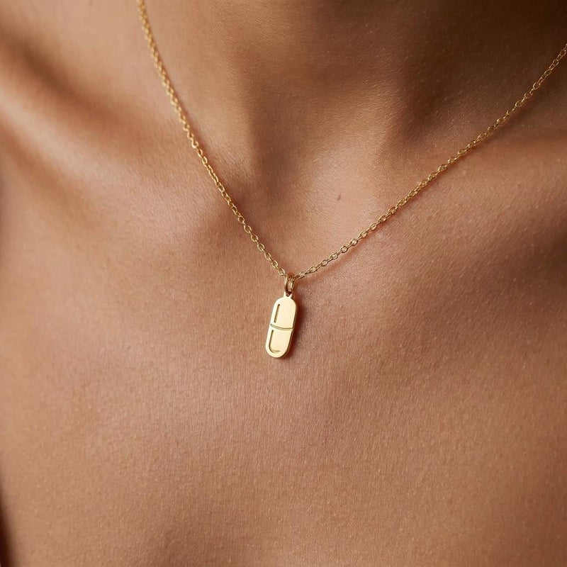 Small gold pill capsule pendant hanging from a fine cable chain.