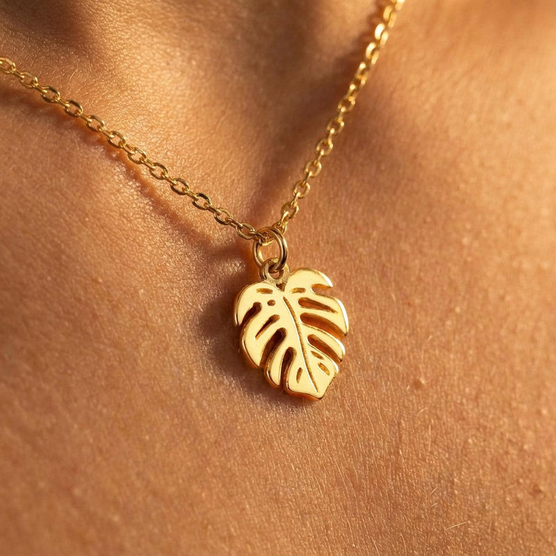 Fine gold chain necklace with a small split monstera leaf pendant on a plain background