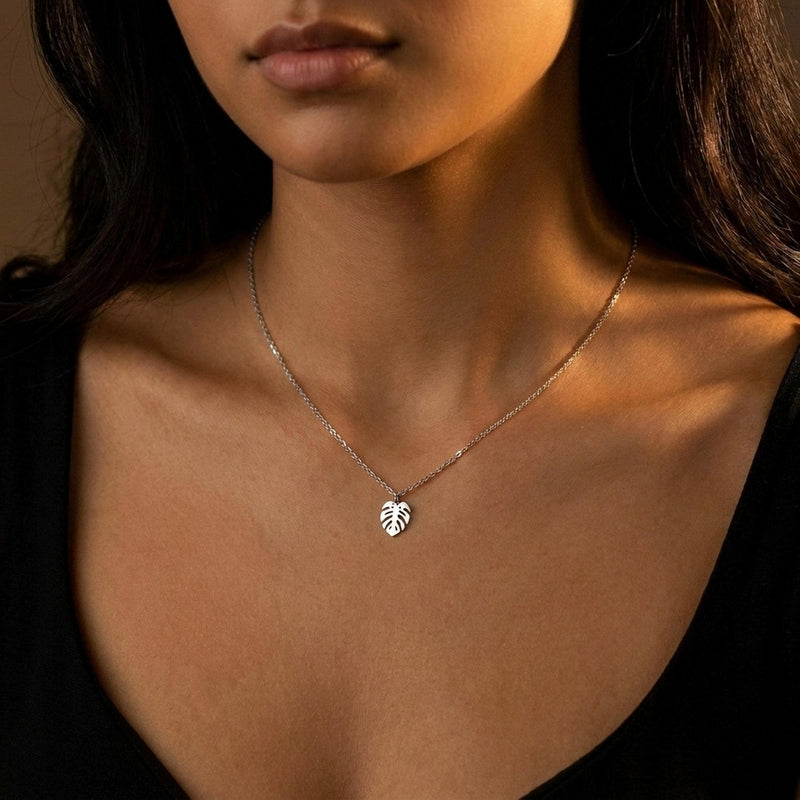 Fine gold chain necklace with a small split monstera leaf pendant on a plain background (2 of 8)